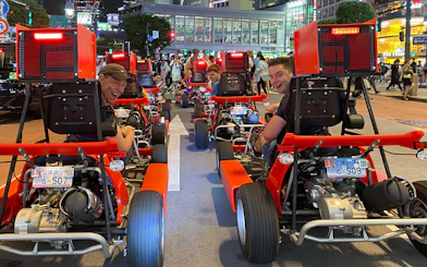 Go-kart riders on Shibuya street during 1-hour tour, Tokyo cityscape in background.