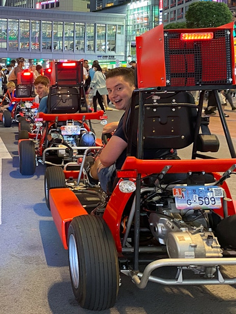 Go-kart riders on Shibuya street during 1-hour tour, Tokyo cityscape in background.