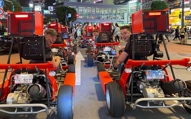 Go-kart riders on Shibuya street during 1-hour tour, Tokyo cityscape in background.