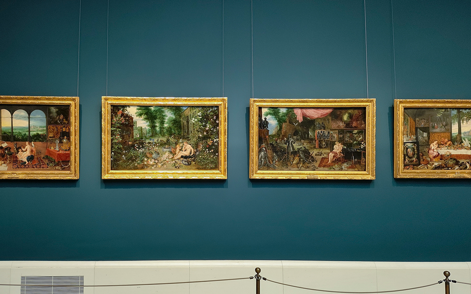 Four framed paintings displayed on a blue wall at Prado Museum, Madrid.