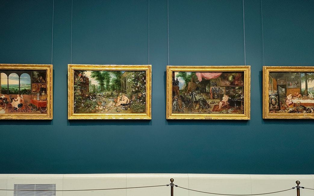 Four framed paintings displayed on a blue wall at Prado Museum, Madrid.