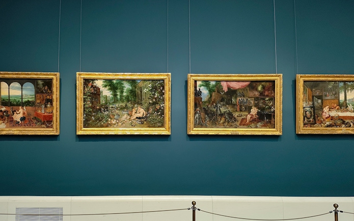 Four framed paintings displayed on a blue wall at Prado Museum, Madrid.