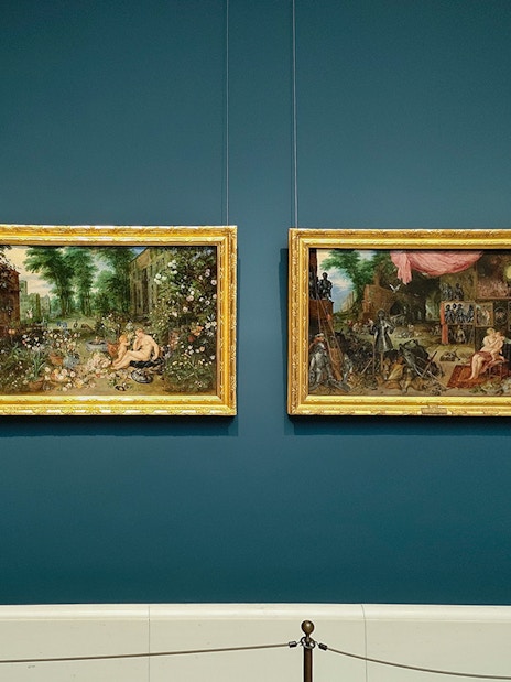 Four framed paintings displayed on a blue wall at Prado Museum, Madrid.