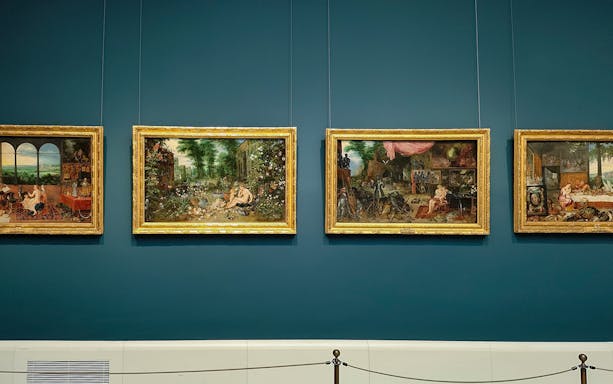 Four framed paintings displayed on a blue wall at Prado Museum, Madrid.