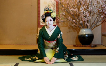 Geisha in traditional kimono kneeling on tatami mat with cherry blossoms in Kyoto.