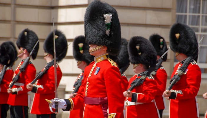 Guards in red uniforms and bearskin hats at Buckingham Palace ceremony.