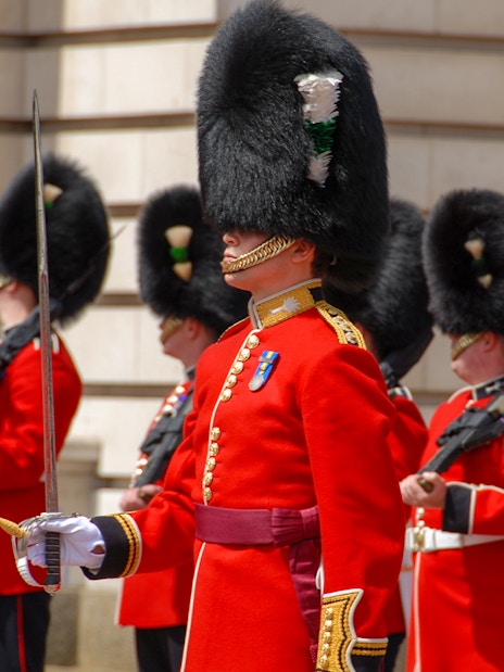 Guards in red uniforms and bearskin hats at Buckingham Palace ceremony.
