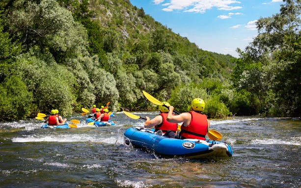Canyoning group paddling through river rapids near Split, surrounded by lush greenery.
