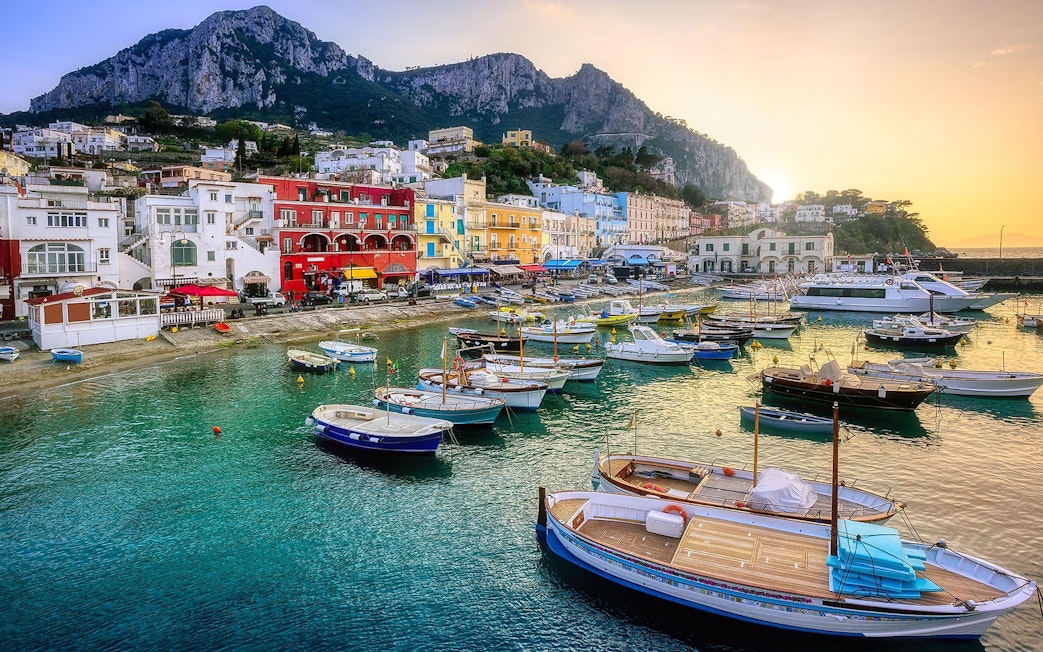 Boats in Marina Grande, Capri Island, with colorful buildings and cliffs in the background.