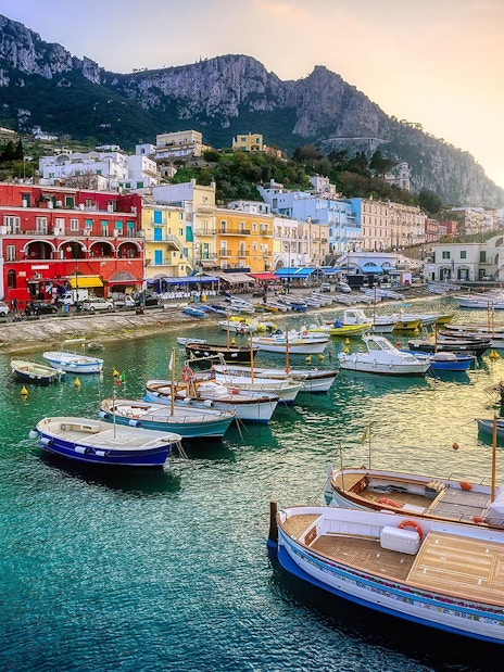 Boats in Marina Grande, Capri Island, with colorful buildings and cliffs in the background.