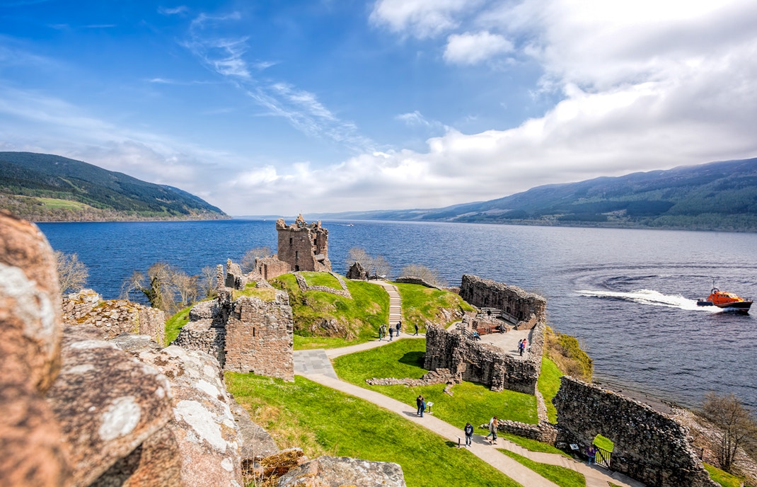 Urquhart Castle ruins overlooking Loch Ness with a boat on the water.