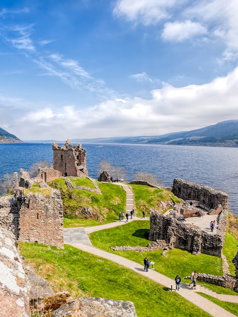 Urquhart Castle ruins overlooking Loch Ness with a boat on the water.