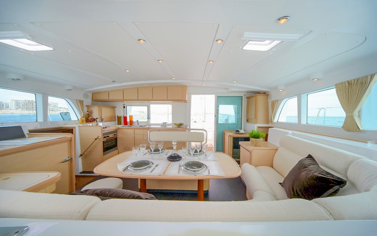 Interior of Santorini sailing catamaran with dining table and sea view.