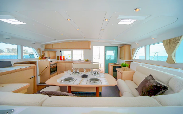 Interior of Santorini sailing catamaran with dining table and sea view.