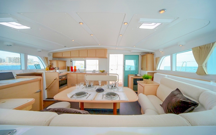 Interior of Santorini sailing catamaran with dining table and sea view.