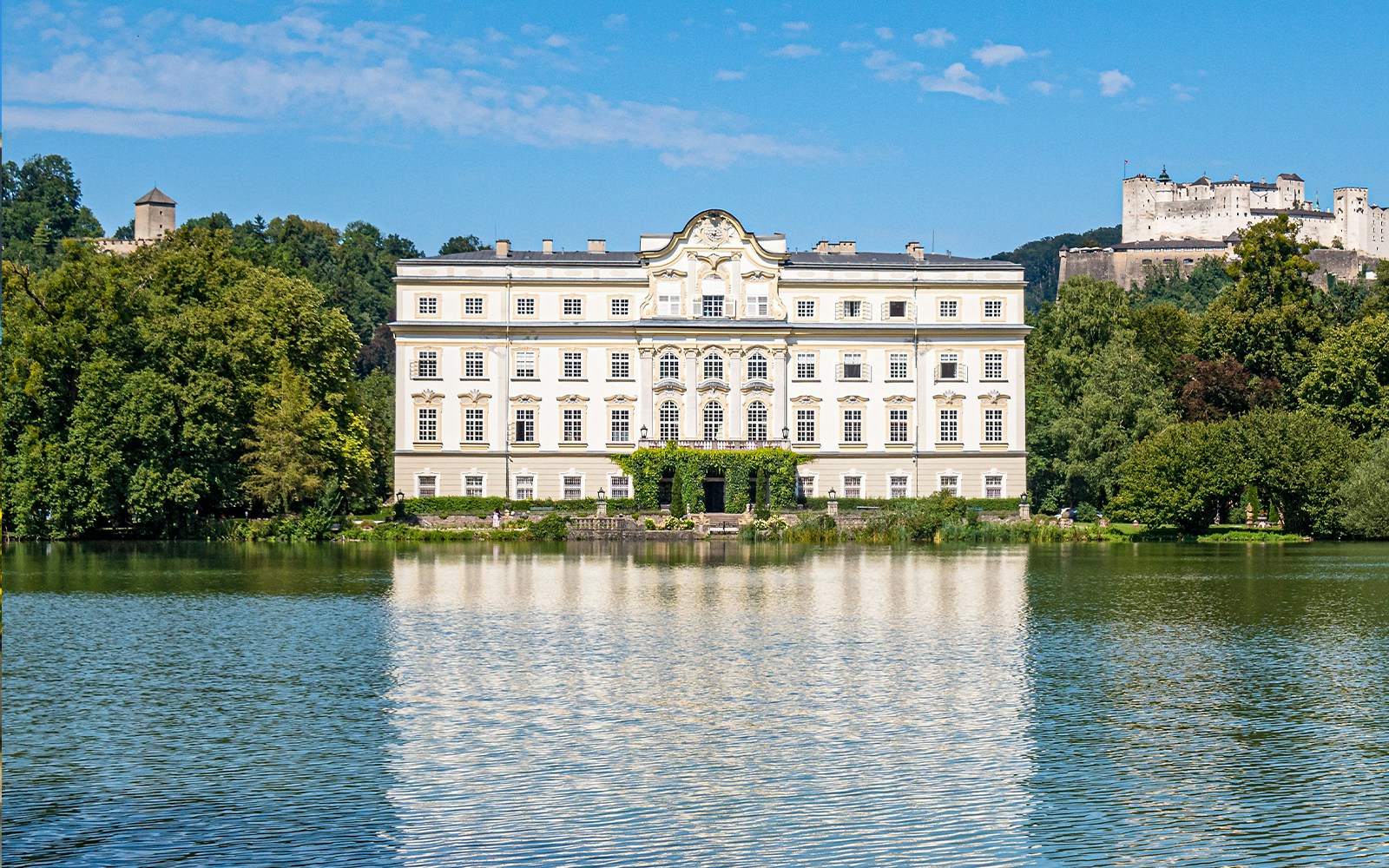 Schloss Leopoldskron reflecting in a lake with Hohensalzburg Fortress in Salzburg.