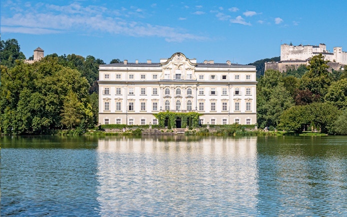 Schloss Leopoldskron reflecting in a lake with Hohensalzburg Fortress in Salzburg.
