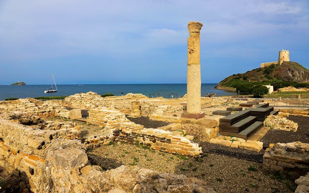 Nora Archaeological Site ruins with sea view and distant tower in Sardinia.