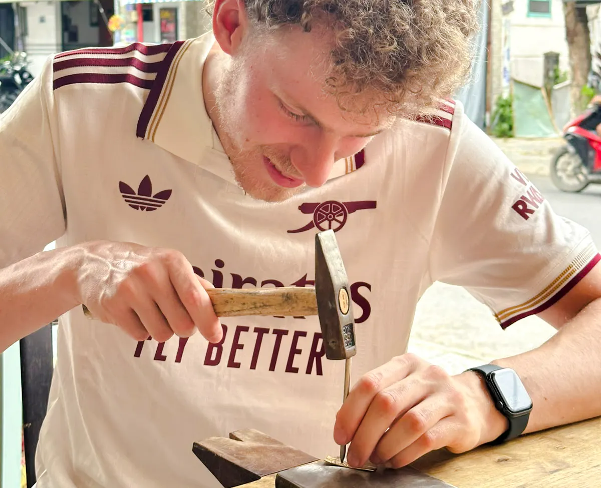 Man crafting jewelry with a hammer in Hoi An workshop.