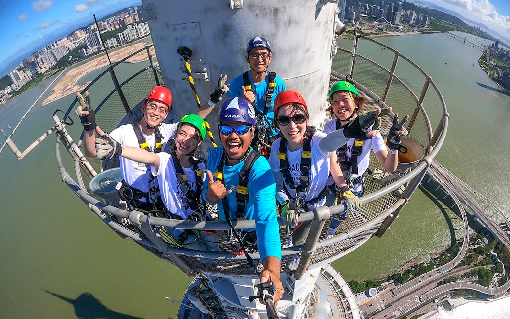 Group of people in harnesses on Skypark Macau tower with city and river view.