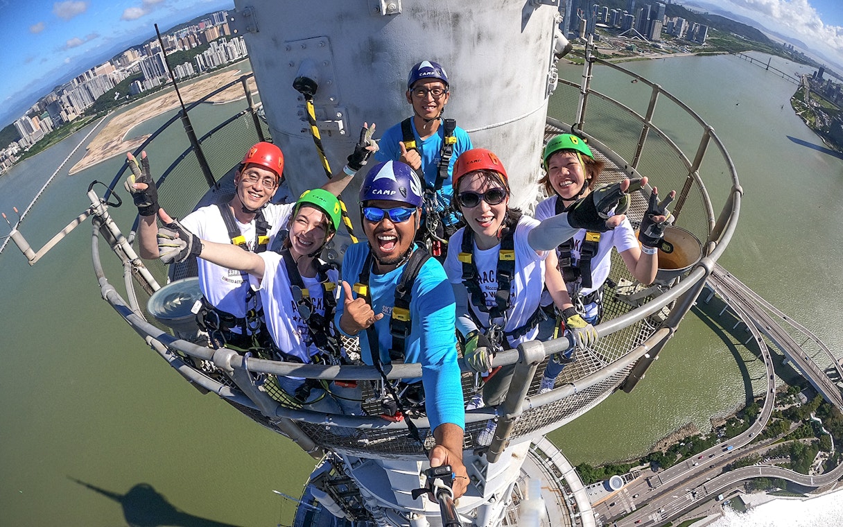 Group of people in harnesses on Skypark Macau tower with city and river view.