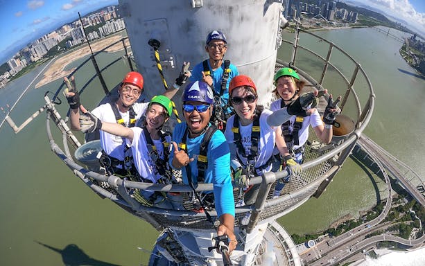 Group of people in harnesses on Skypark Macau tower with city and river view.