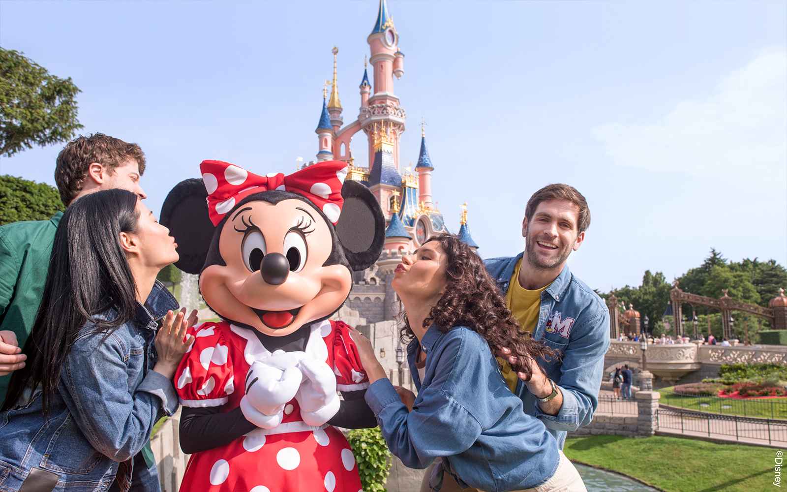 Guests posing with Minnie Mouse at Disneyland Paris with Sleeping Beauty Castle in the background.