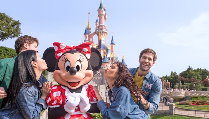 Guests posing with Minnie Mouse at Disneyland Paris with Sleeping Beauty Castle in the background.