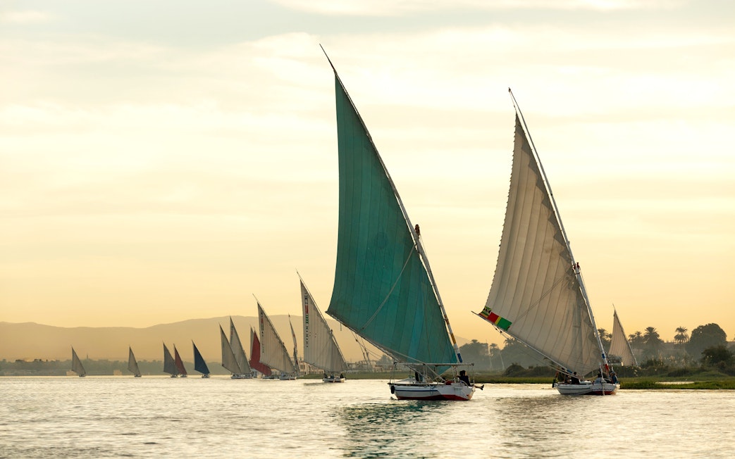 Traditional felucca boats sailing on the Nile River at sunset in Aswan.