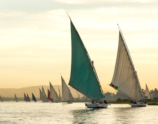 Traditional felucca boats sailing on the Nile River at sunset in Aswan.