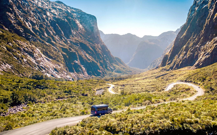 Minibus on scenic road through Milford Sound mountains, part of small group tour from Queenstown.