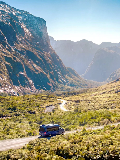 Minibus on scenic road through Milford Sound mountains, part of small group tour from Queenstown.