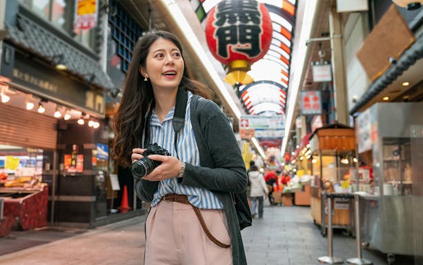 Tourist exploring vibrant market street in Osaka with camera.