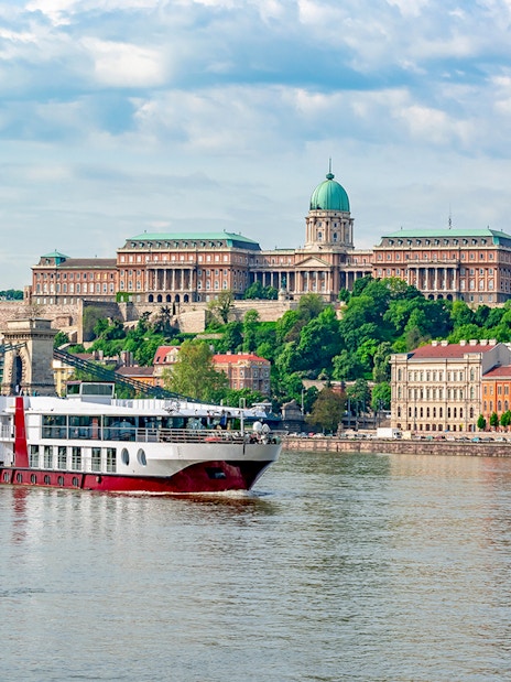 Cruise ship on the Danube River with Buda Castle in Budapest.