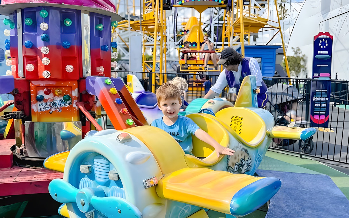 Child smiling on a colorful airplane ride at Luna Park.