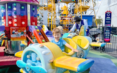 Child smiling on a colorful airplane ride at Luna Park.