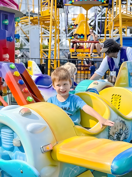 Child smiling on a colorful airplane ride at Luna Park.