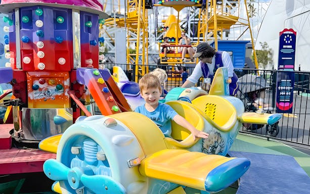 Child smiling on a colorful airplane ride at Luna Park.