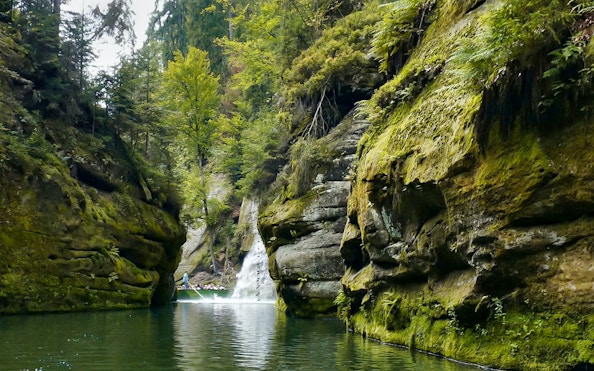 Boat navigating through rocky gorge with waterfall, part of Bastei Bridge guided tour.