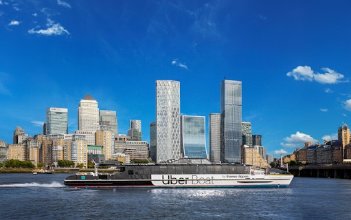 Uber Boat on Thames River passing Canary Wharf skyscrapers.