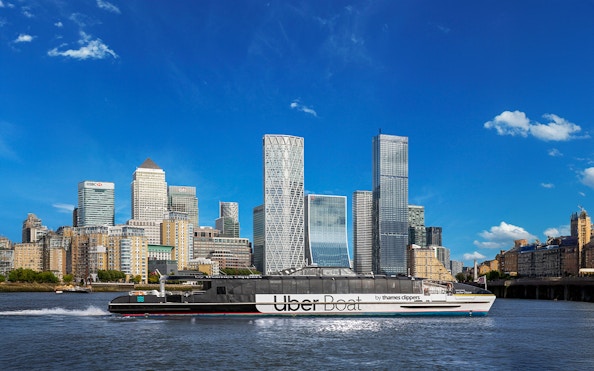 Uber Boat on Thames River passing Canary Wharf skyscrapers.