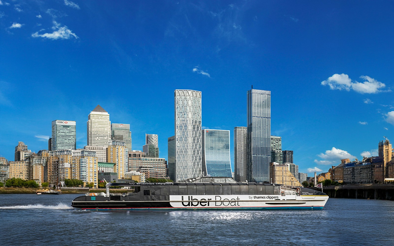 Thames River Uber Boat cruising past Canary Wharf skyscrapers in London.