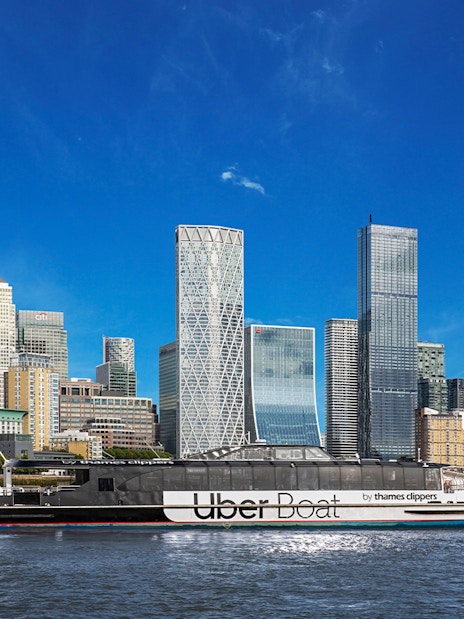 Uber Boat on Thames River passing Canary Wharf skyscrapers.