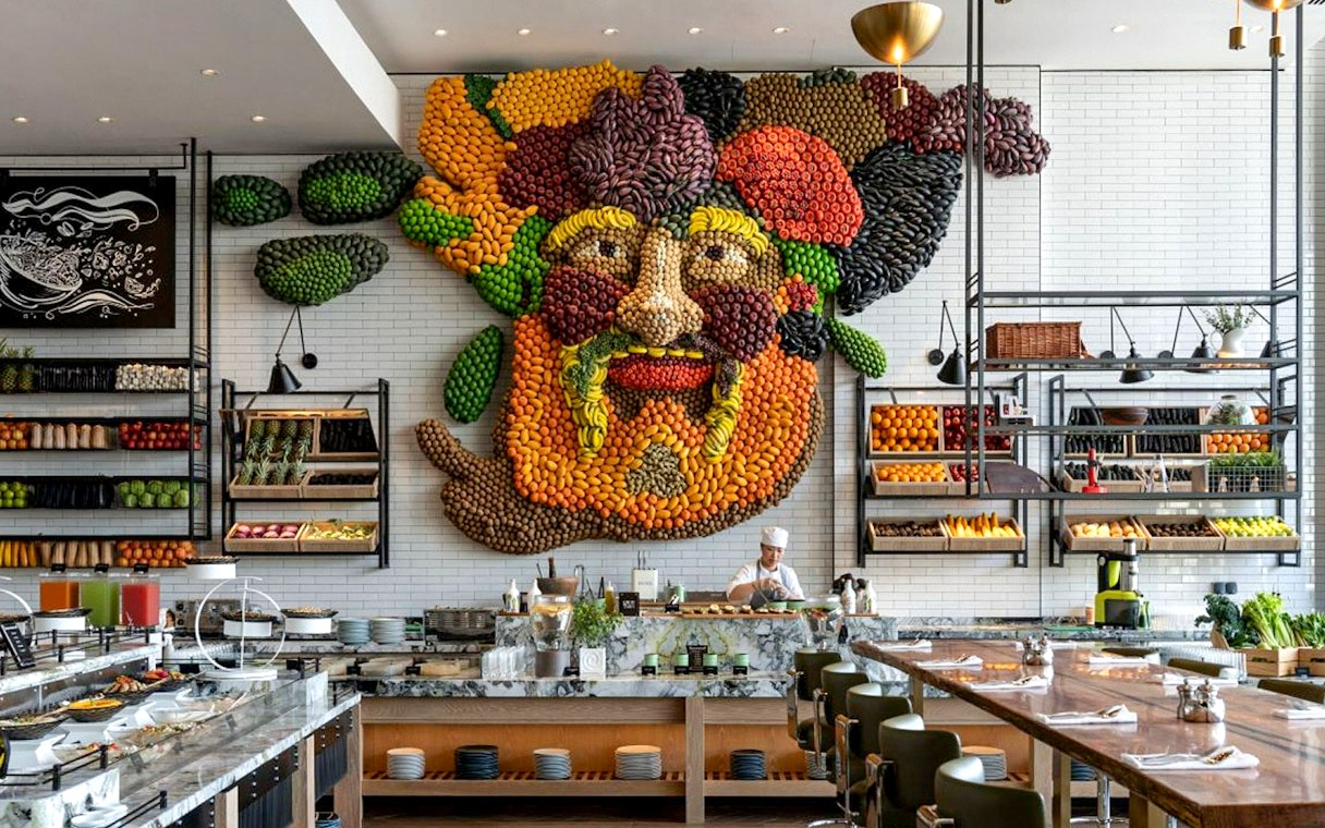 Live cooking station with chef at Gastronomy Buffet Dinner, Dubai, featuring vibrant fruit and vegetable wall art.
