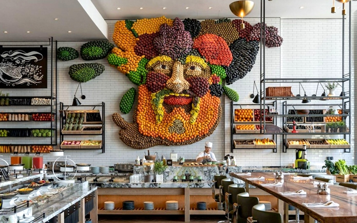 Live cooking station with chef at Gastronomy Buffet Dinner, Dubai, featuring vibrant fruit and vegetable wall art.