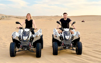 Two people riding quad bikes on a desert safari in Abu Dhabi.