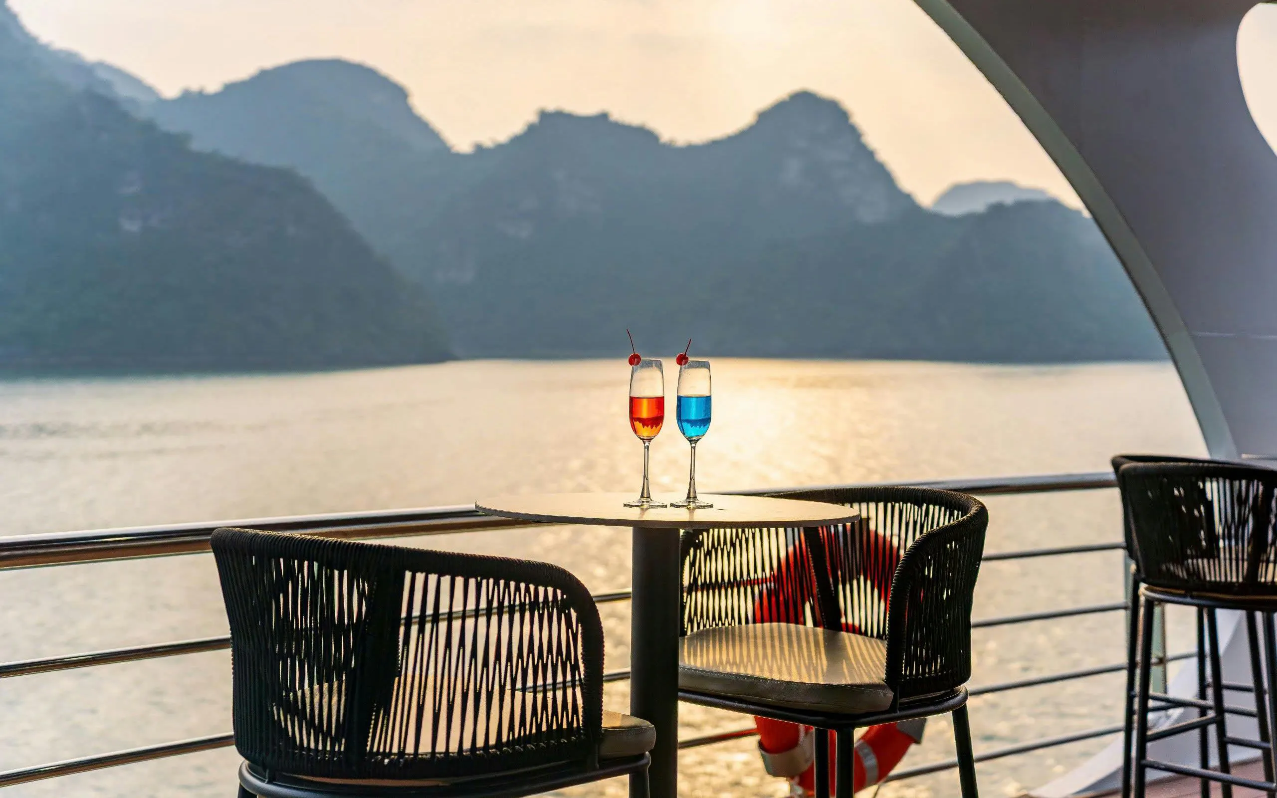 Luxury cruise deck with drinks overlooking Ha Long Bay at sunset.