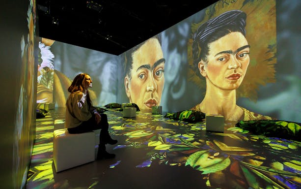Frida Kahlo's portraits projected in immersive exhibition with visitor seated.