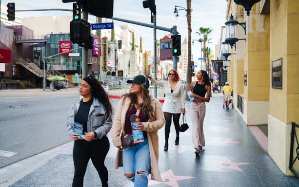 Guests walking along the Hollywood Walk of Fame on a self-guided tour, holding brochures.