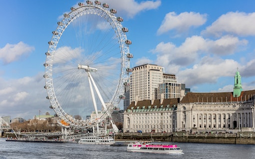London Eye and river cruise boat on the Thames with cityscape in the background.